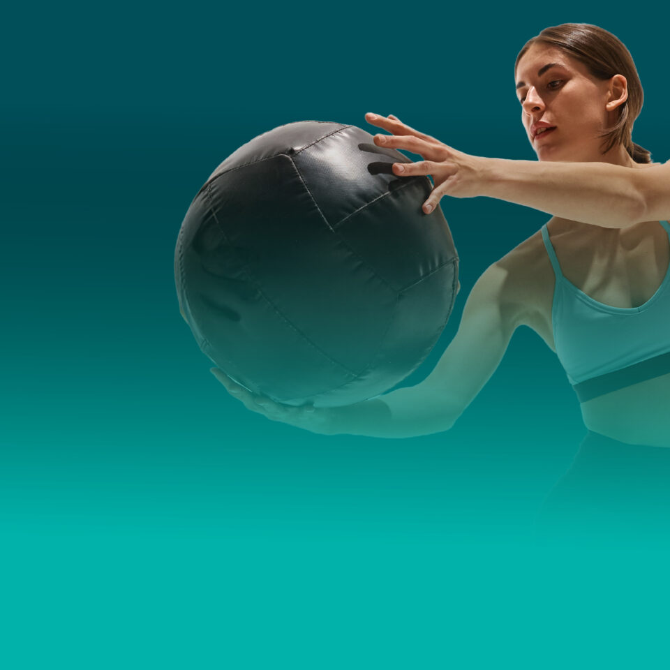 Female Athlete holding medicine ball during functional workout on teal background